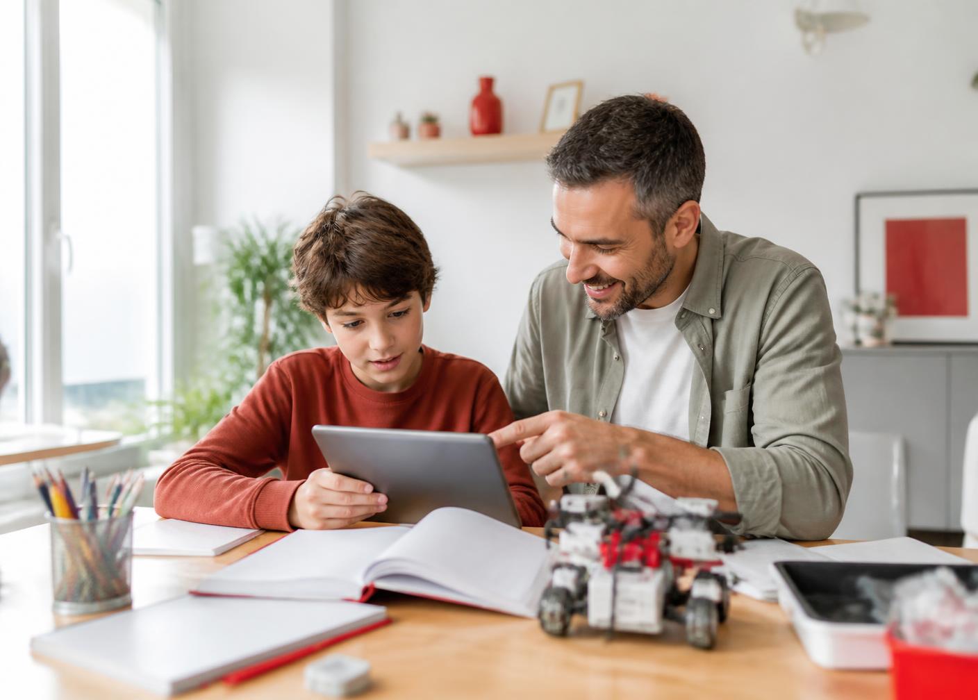 A parent and child learning together at home with a tablet, notebooks and a robotics kit